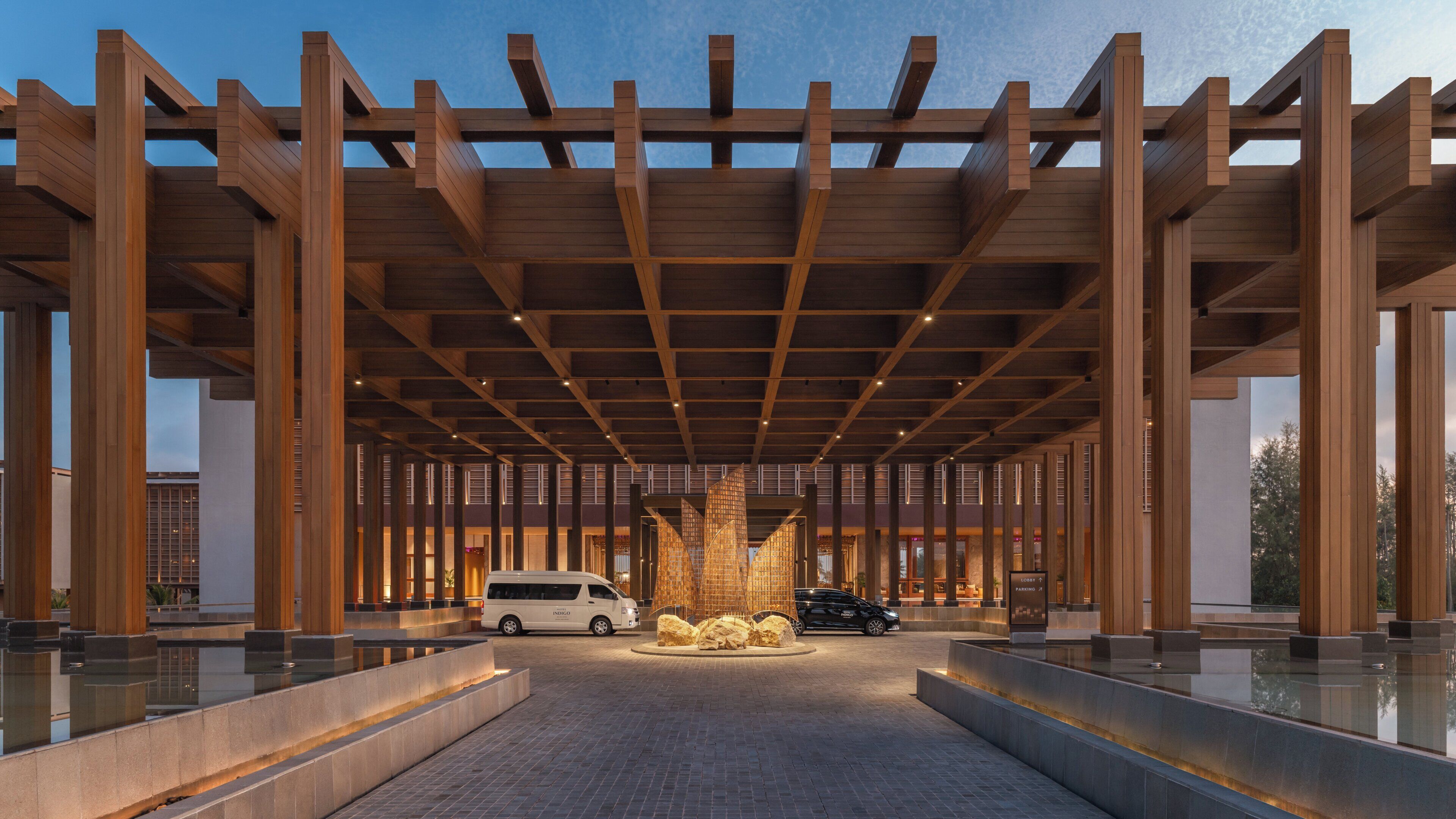 A modern building with a wooden structure, a central water feature, and a paved entrance.
