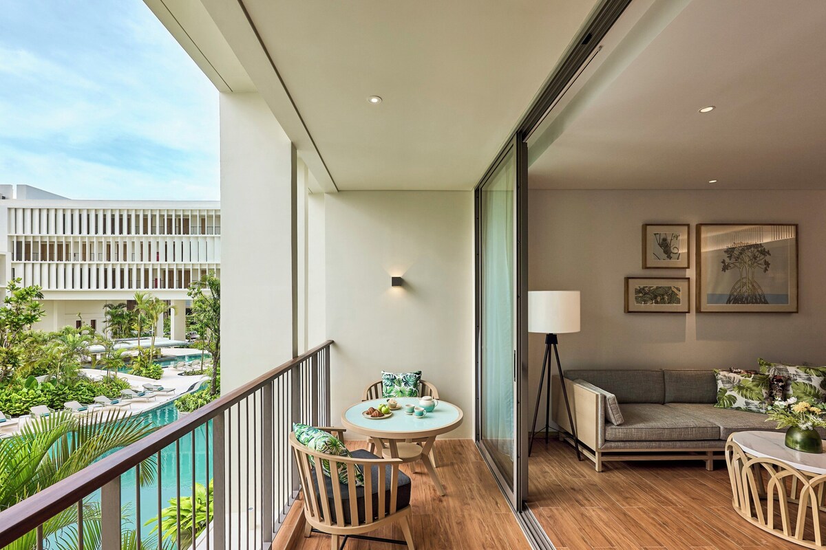A balcony with a pool view, a dining area with a table and chairs, a sofa, and a lamp.