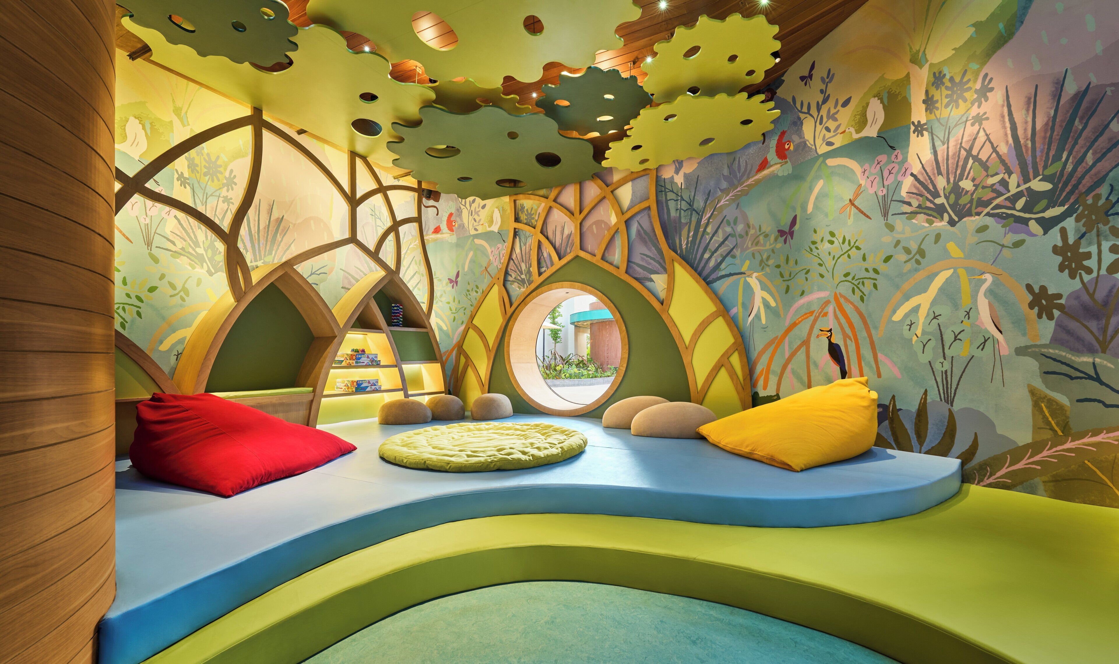 Een kinderspeelruimte met kleurrijke muurschilderingen, een rond raam en zachte zitplaatsen.