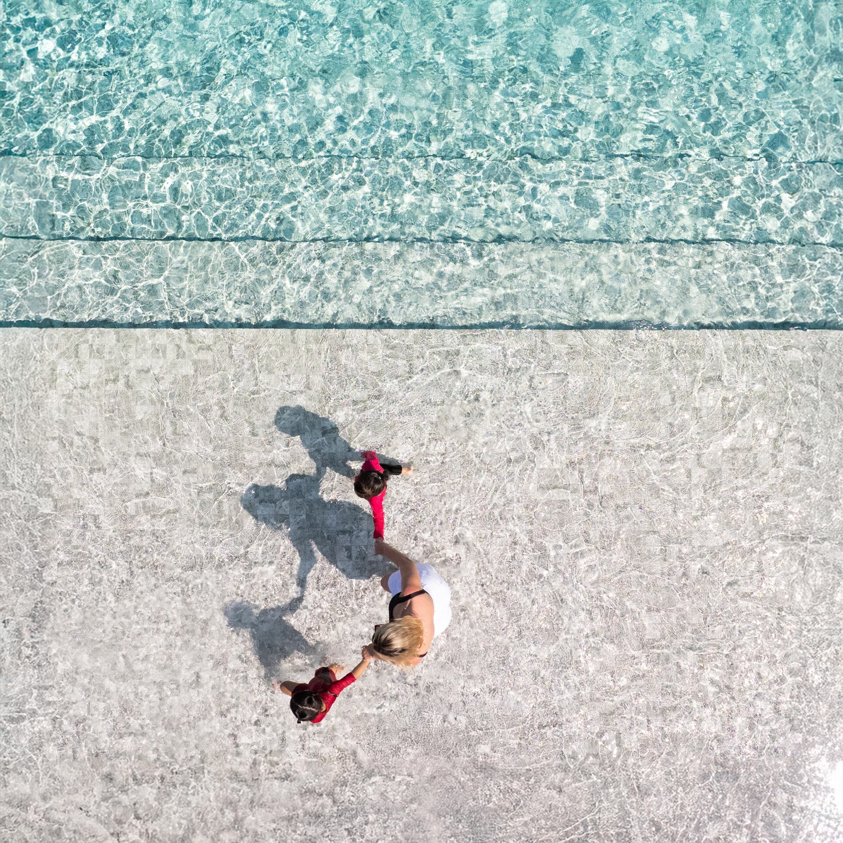 An aerial view of a beach with clear shallow water and a sandy shore.