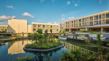 A hotel with a central courtyard featuring a reflective water pond, surrounded by lush greenery and modern buildings with balconies.
