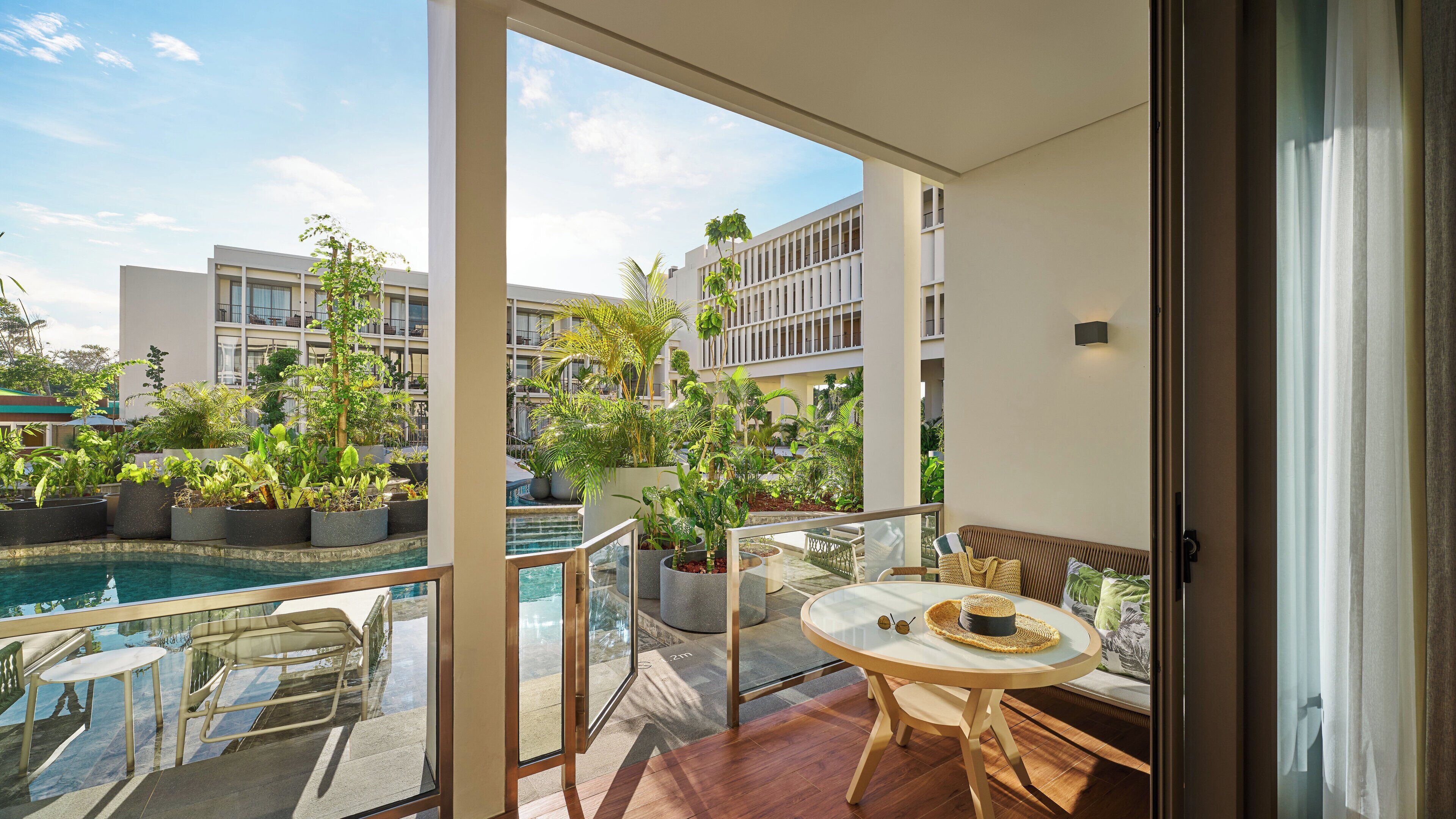 A balcony with a pool, potted plants, and a seating area with a table and chairs.