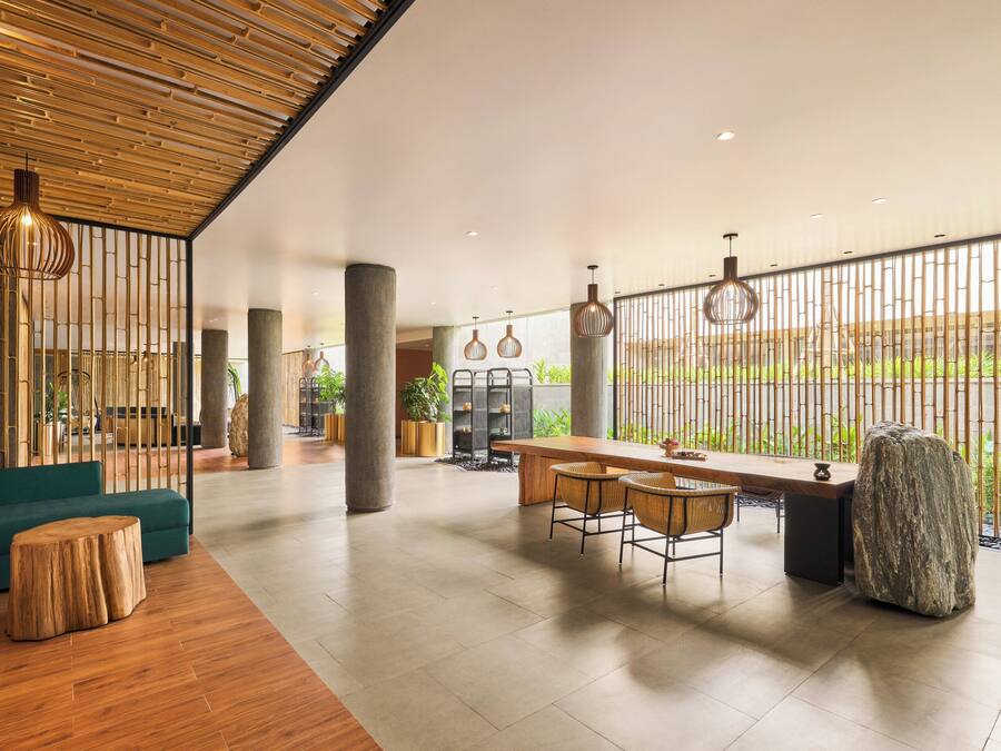 A spacious lobby with a wooden ceiling, a green sofa, a wooden dining table with chairs, and a large window with a view of greenery.
