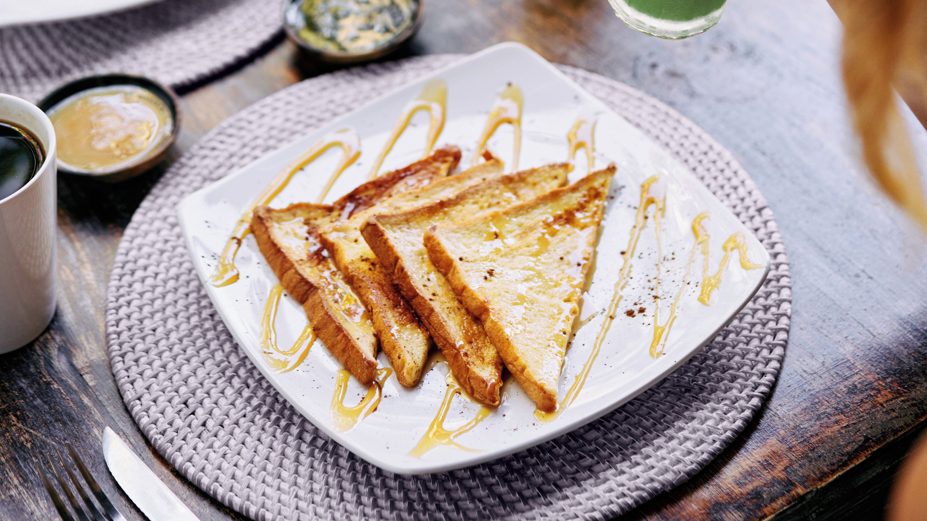 A plate of toasted bread with honey drizzles on a woven placemat.