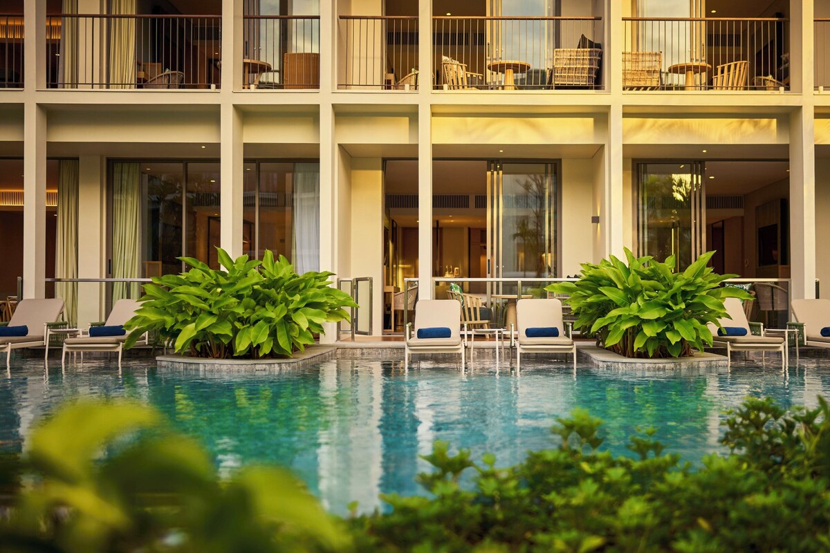 A hotel with a pool area, lounge chairs, and a view of the building's interior.