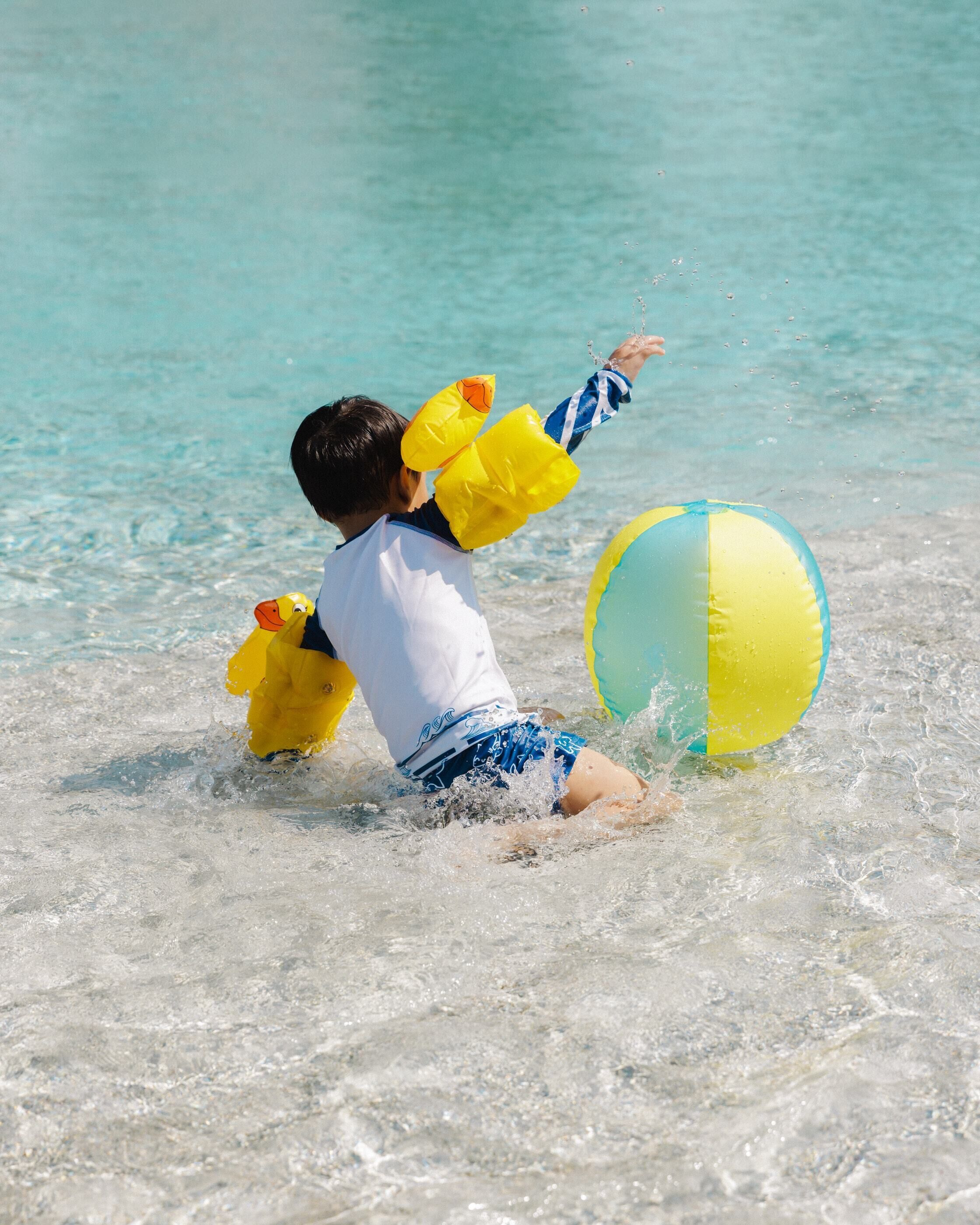 A child playing with a beach ball and duck floaties at the beach.