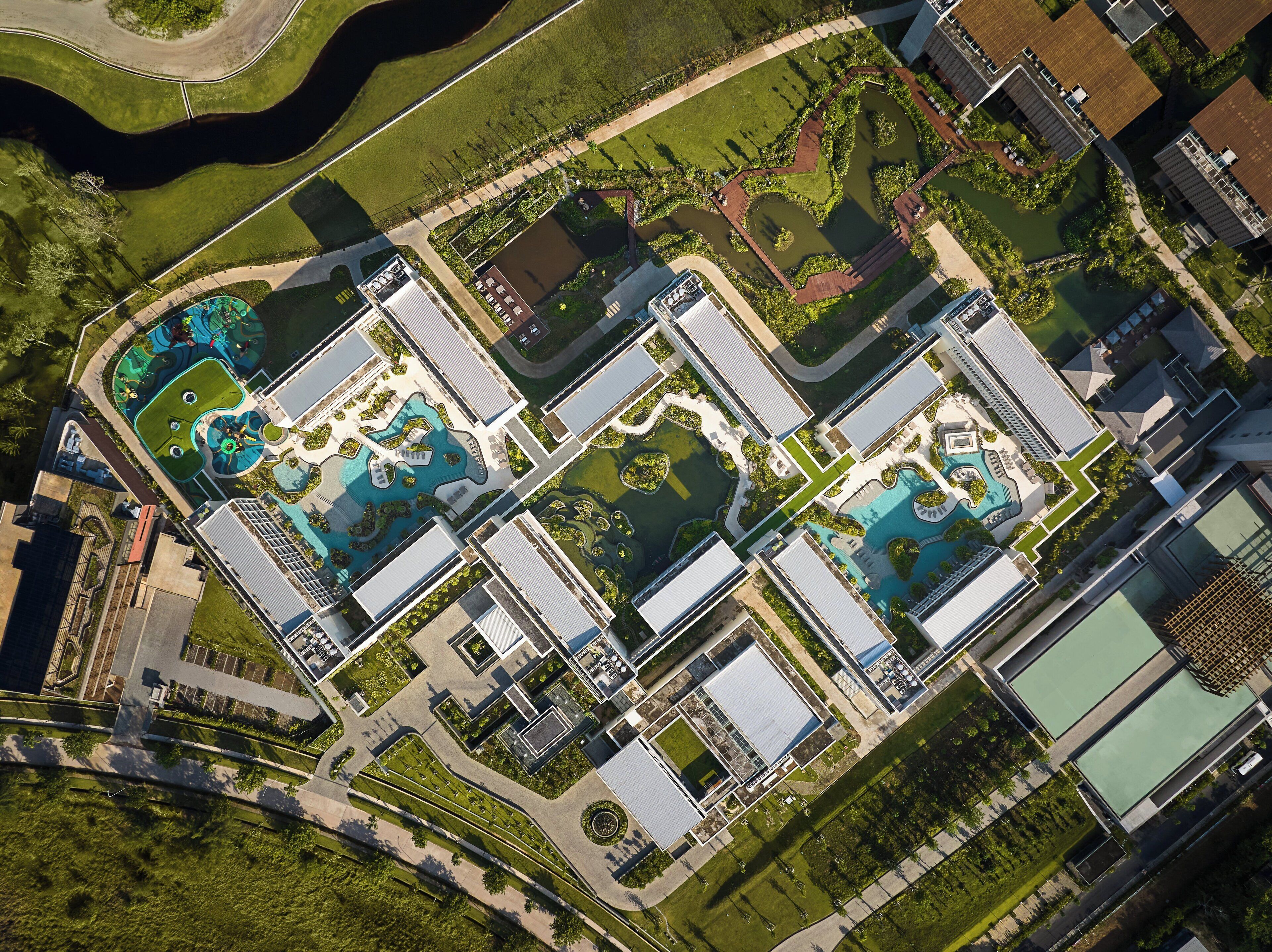 Vue aérienne d’un complexe hôtelier moderne comprenant plusieurs bâtiments, des jardins aménagés et des piscines.