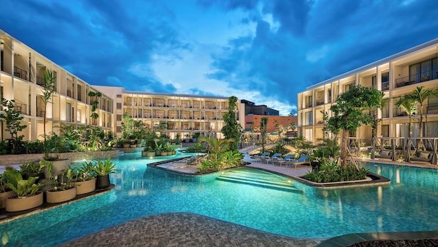 Un hôtel doté d’une piscine centrale, entourée d’une végétation luxuriante et agrémenté de nombreux balcons.