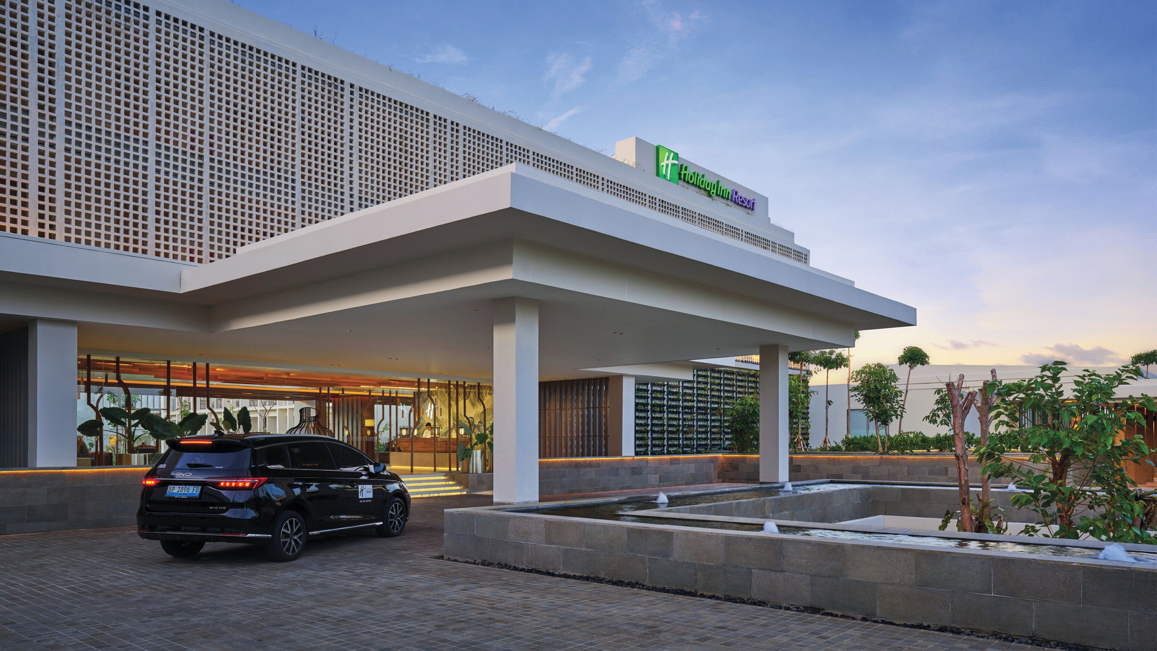 A modern hotel with a large entrance, a covered waiting area, and a water feature in front.