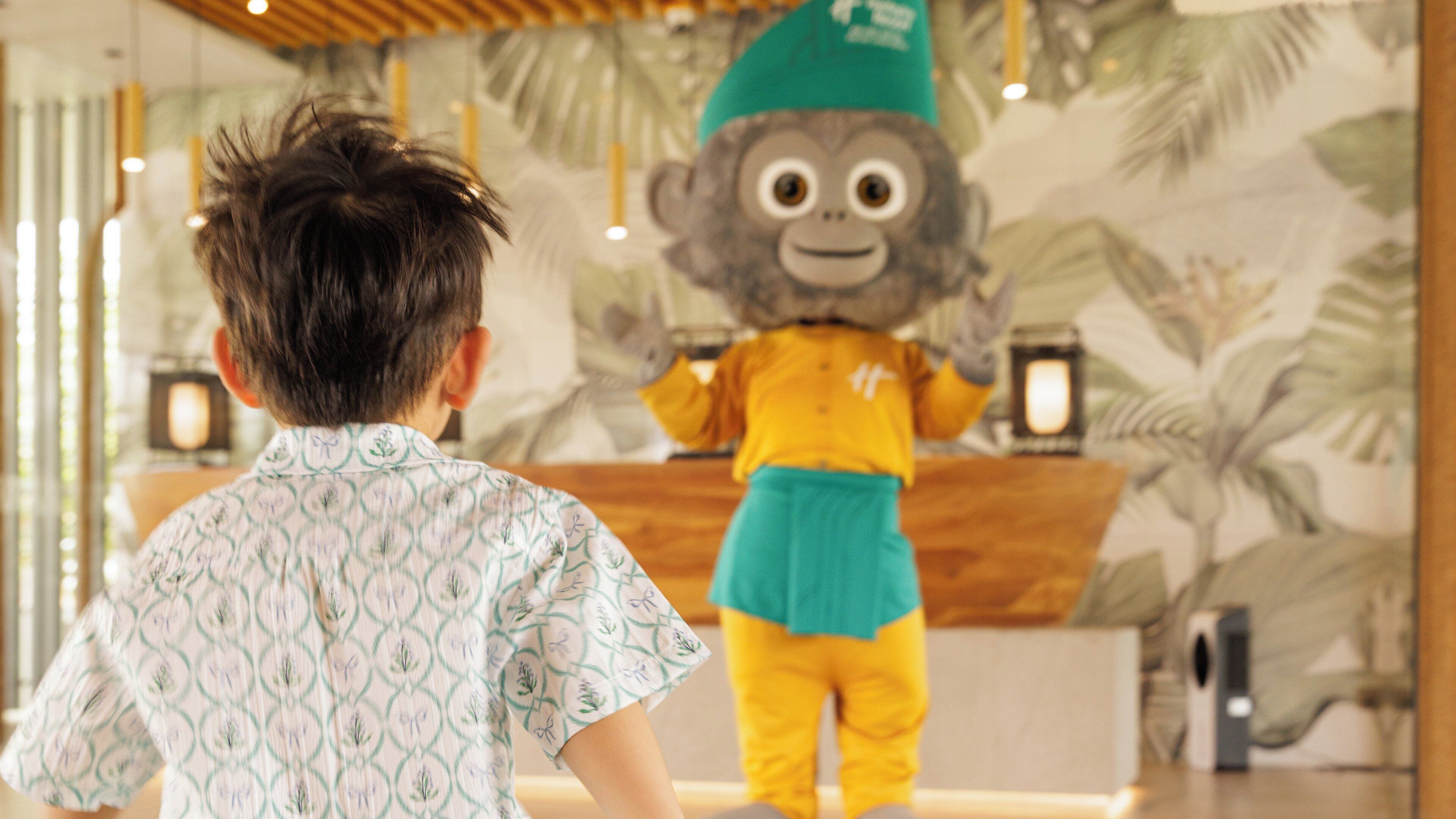A child facing a mascot with a tropical-themed backdrop.