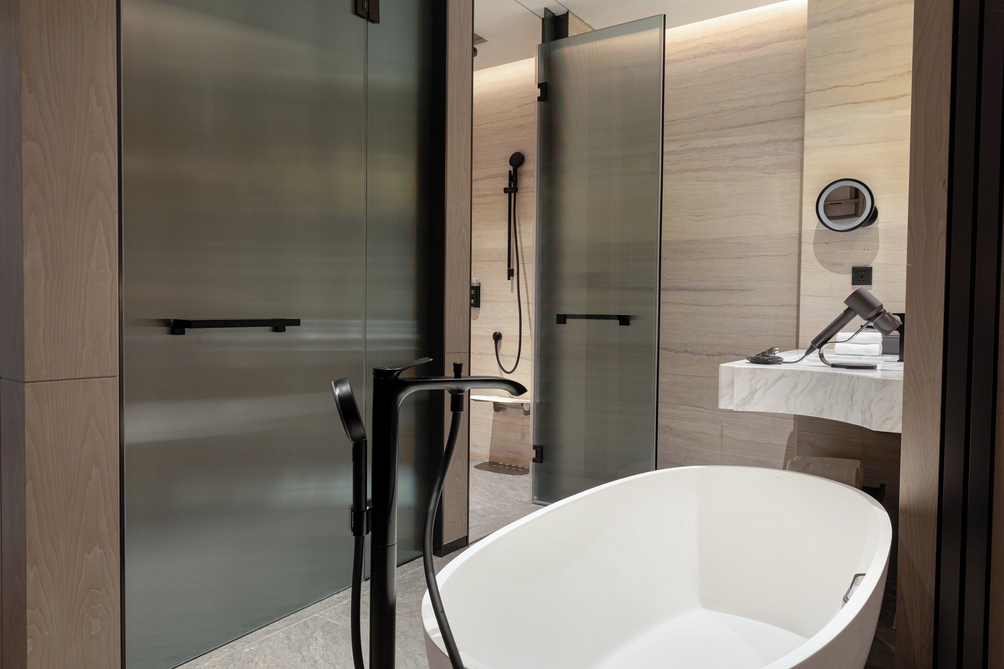 A modern bathroom with a freestanding bathtub, a glass shower enclosure, and a marble countertop with a sink and mirror.
