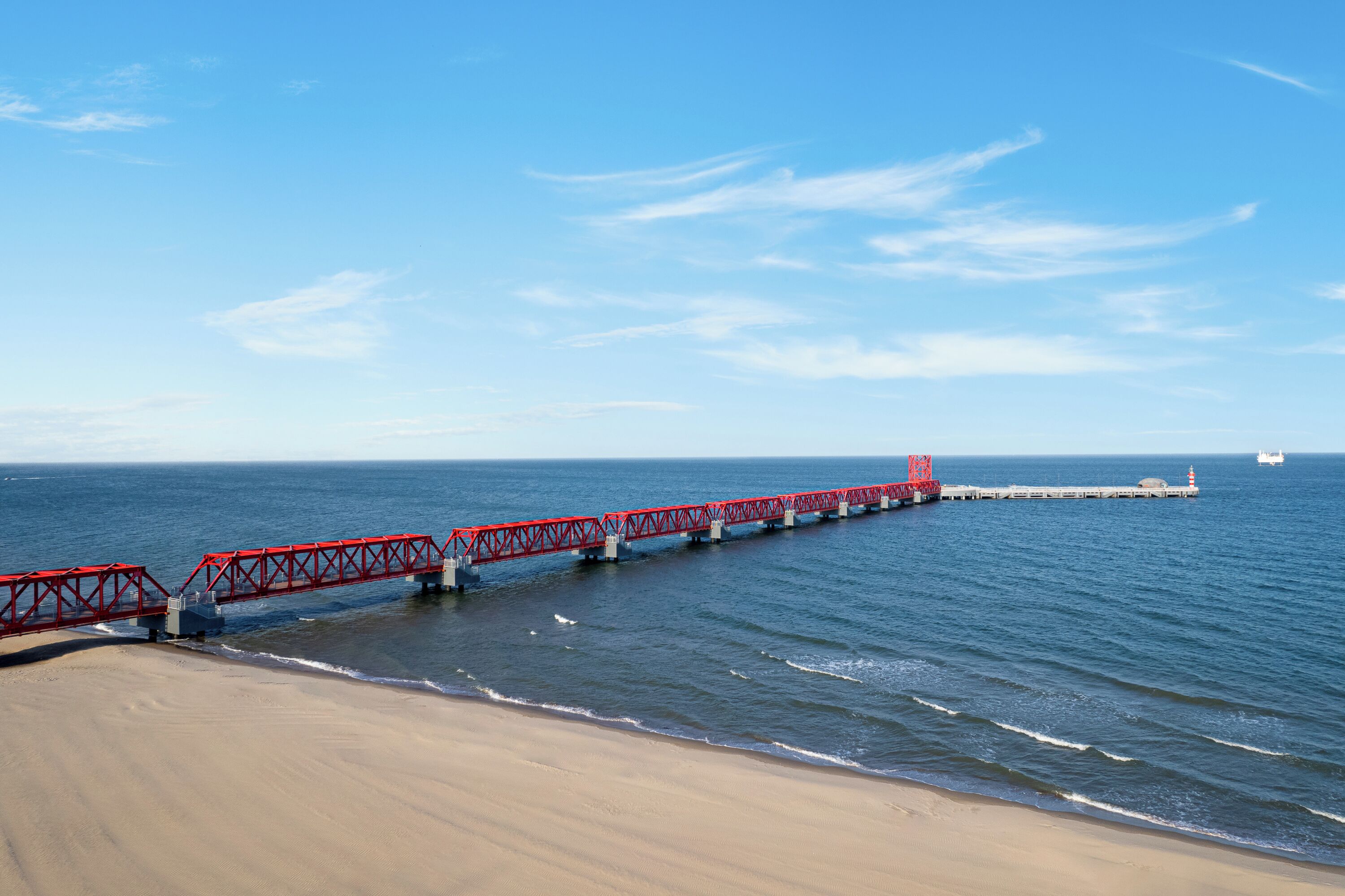 A red pier extending into the ocean with a lighthouse at the end.