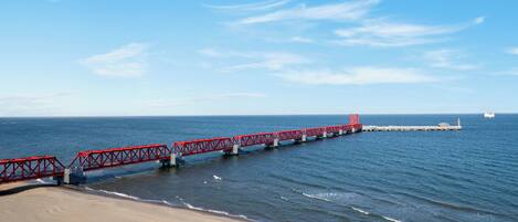 A red pier extending into the ocean with a lighthouse at the end.