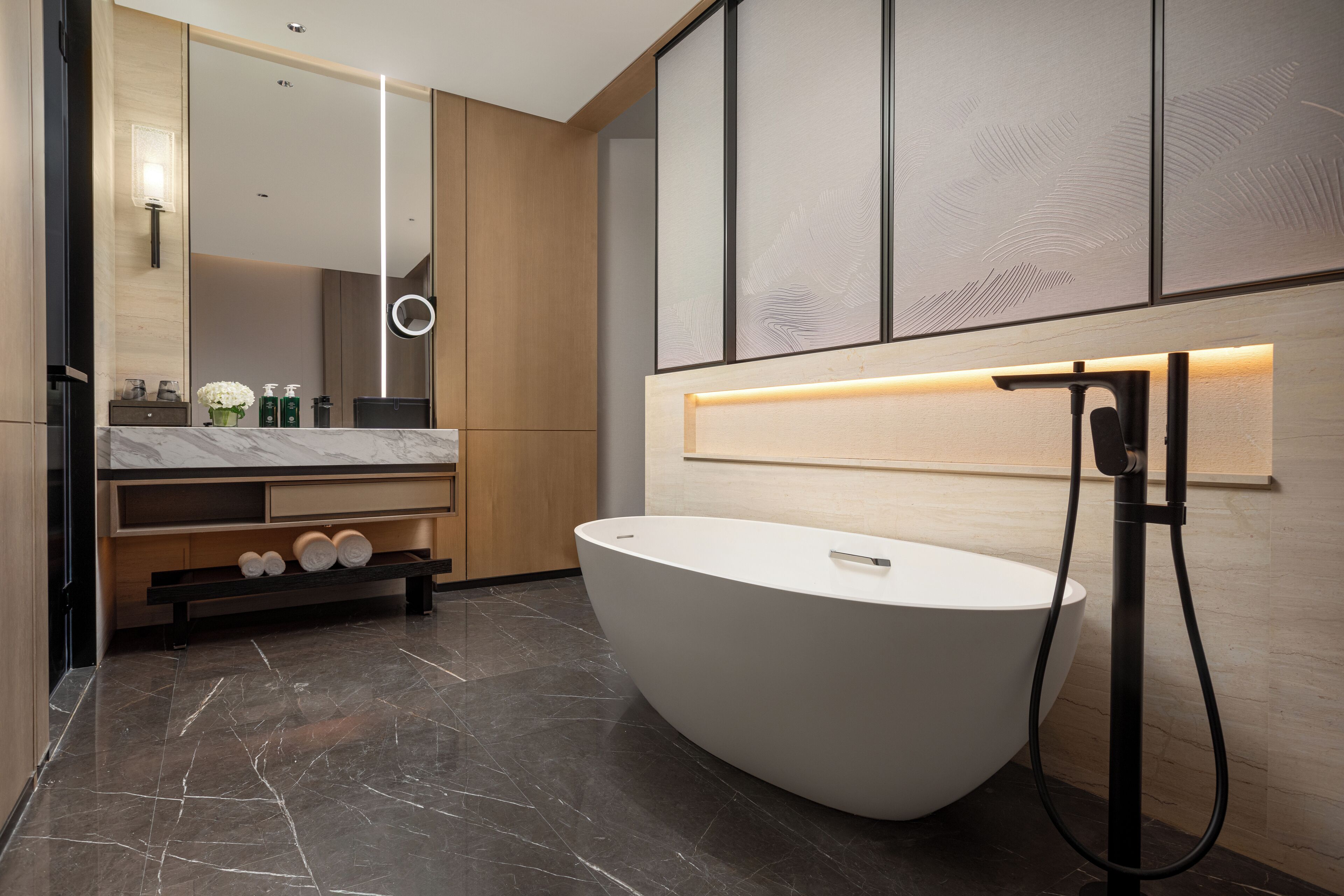 Ein modernes Badezimmer mit einer großzügigen freistehenden Badewanne, einem Waschtisch inklusive Spiegel und einem hängenden Handtuchhalter.