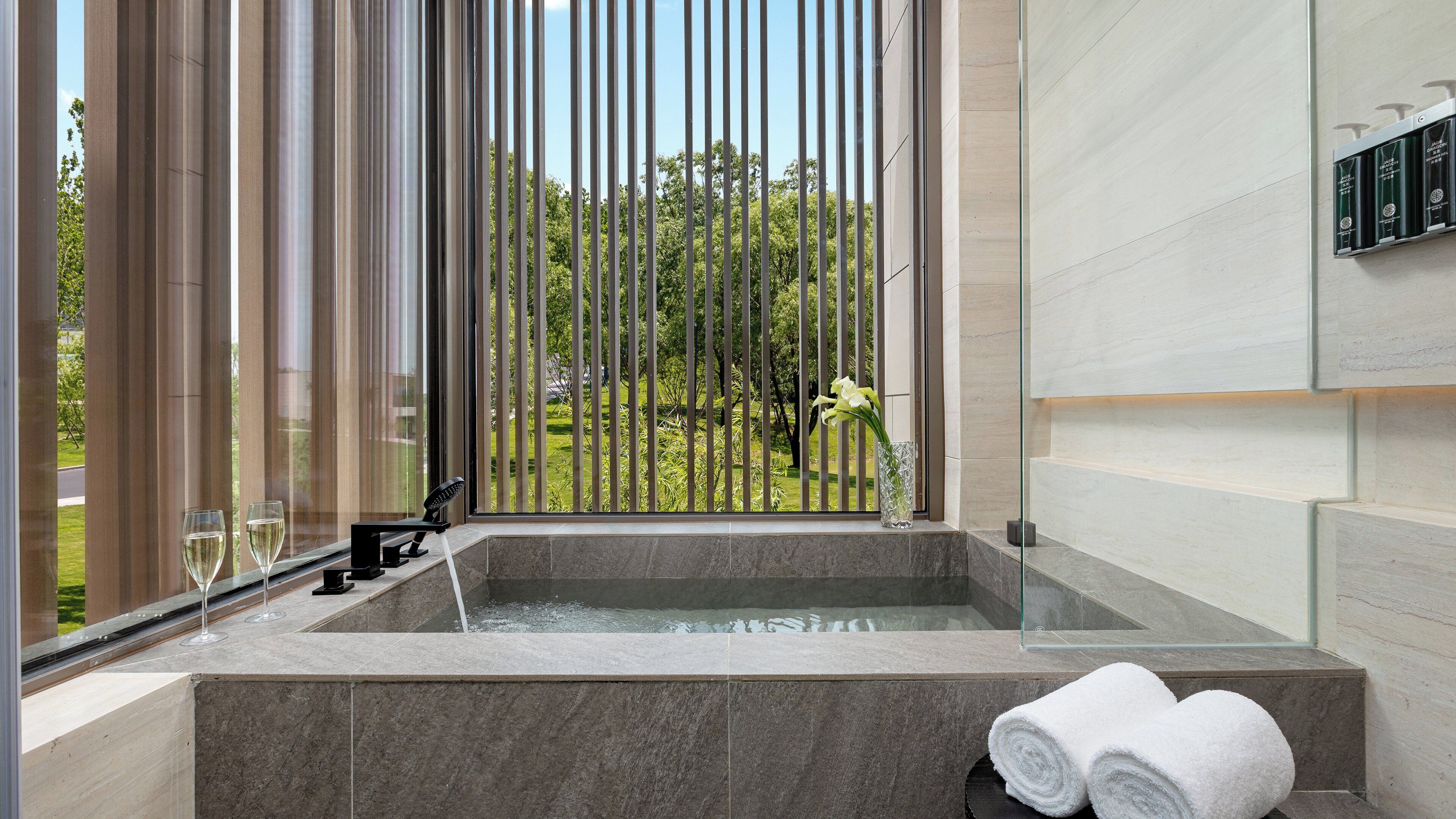 A modern bathroom with a large bathtub, a glass shower enclosure, and a view of a garden.