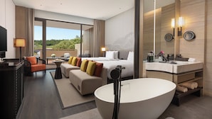 Habitació d'hotel moderna amb un llit gran, zona de seients amb un sofà i butaques, una banyera espaiosa, un tocador amb mirall i una televisió.