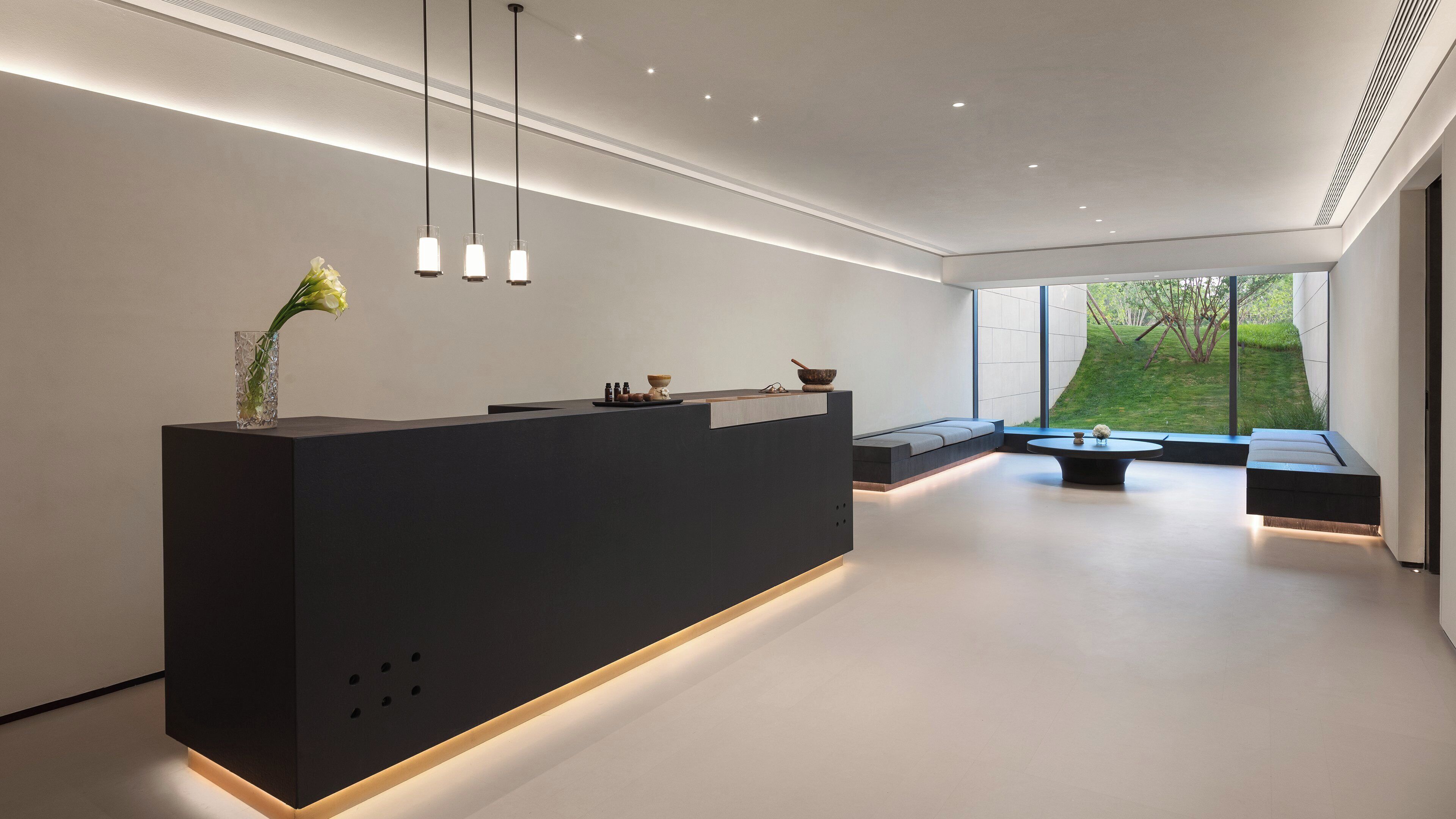 Een moderne receptiebalie met een donker aanrecht, een zithoek met een bank, en een groot raam met uitzicht op de omgeving.