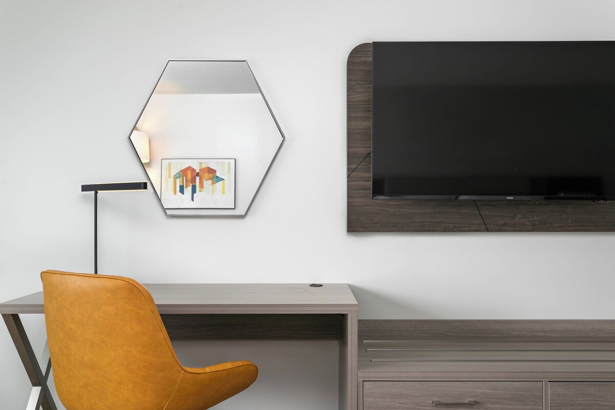 Una camera moderna con una scrivania, una sedia, una TV a parete e un'opera d'arte appesa.
