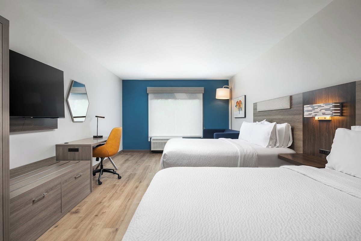 A hotel room with a bed, a desk, a chair, a TV, and a window with curtains.