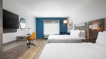 A hotel room with a bed, a desk, a chair, a TV, and a window with curtains.
