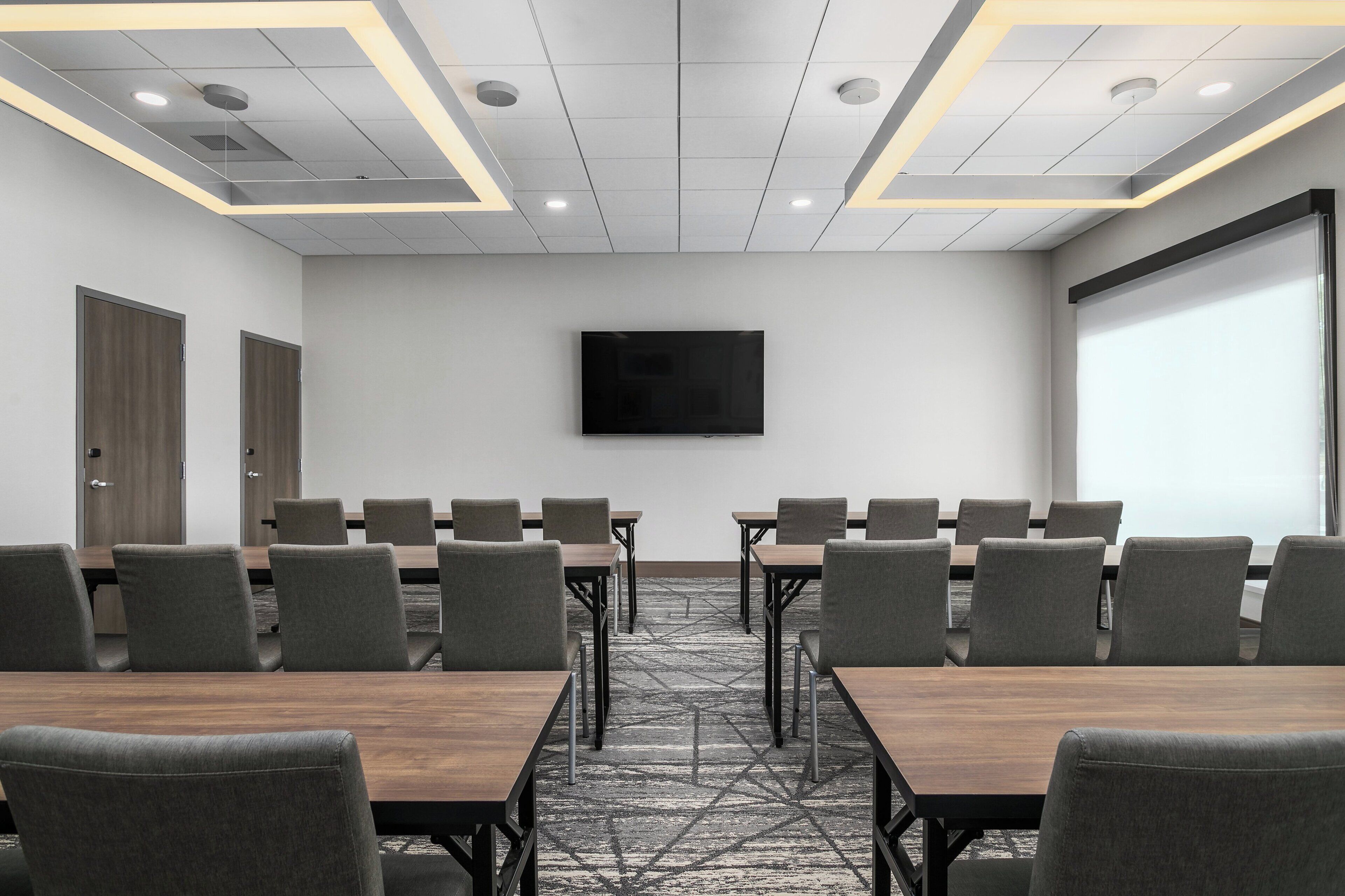 A conference room with a large screen, multiple tables, and chairs arranged for meetings.