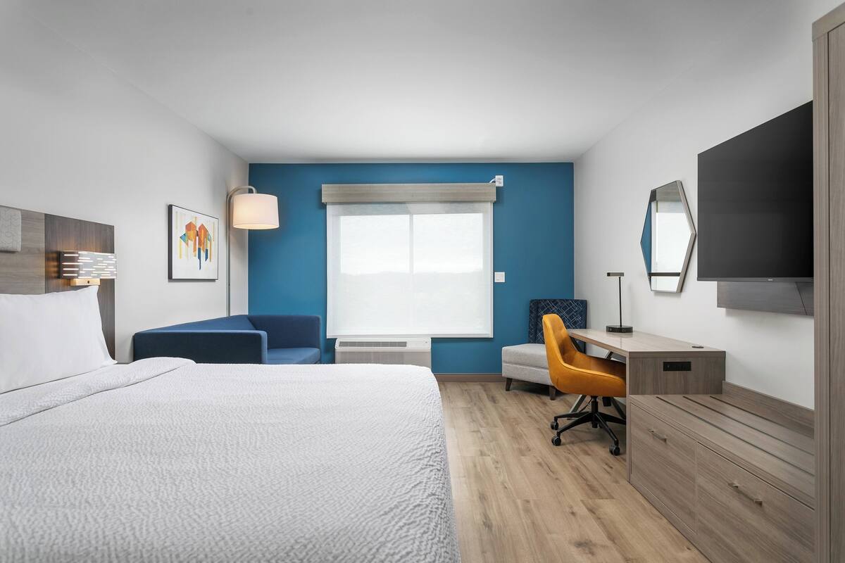 A hotel room with a large bed, a desk, a chair, and a TV.