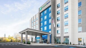 Un hôtel moderne à la façade bleue et grise, doté d’une entrée couverte et d’un parking comprenant des places réservées aux personnes handicapées.