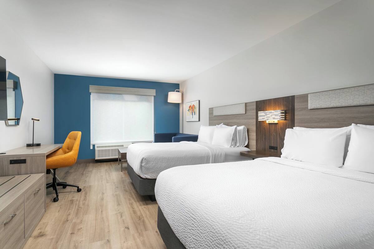 A hotel room with two beds, a desk, a chair, and a window with blinds.