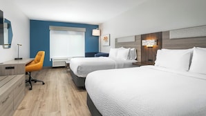 Une chambre d’hôtel avec deux lits, un bureau, une chaise et une fenêtre avec des stores.