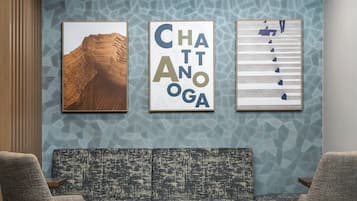 Una habitación con un papel tapiz estampado, un sofá y dos sillones. Se observan tres cuadros enmarcados en la pared.