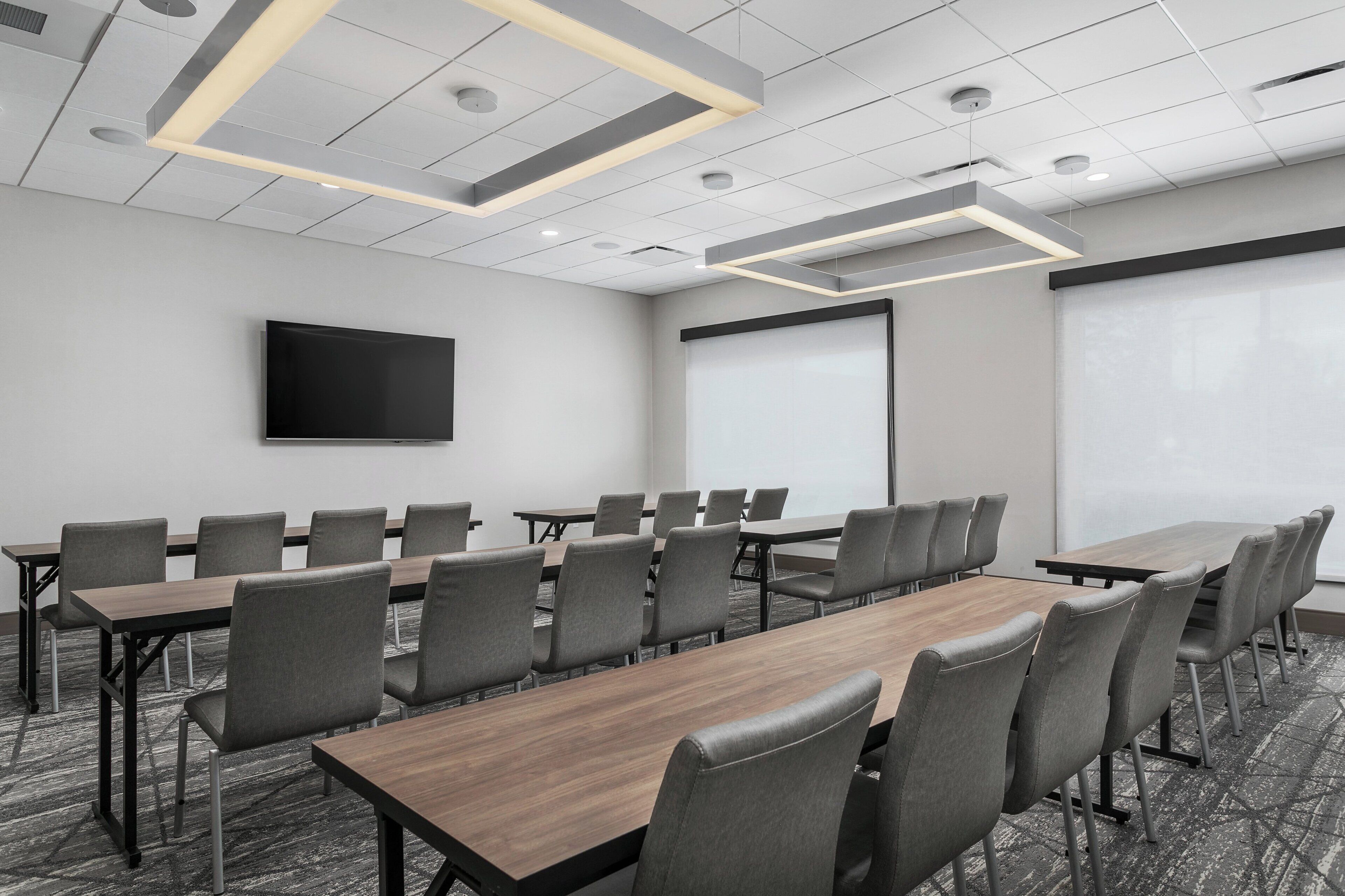 A conference room with long tables and chairs, a flat-screen TV, a projector screen, and a whiteboard.