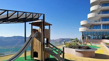 Children can play on the slide and in the playhouse, surrounded by a green carpeted area with a view of the mountains.