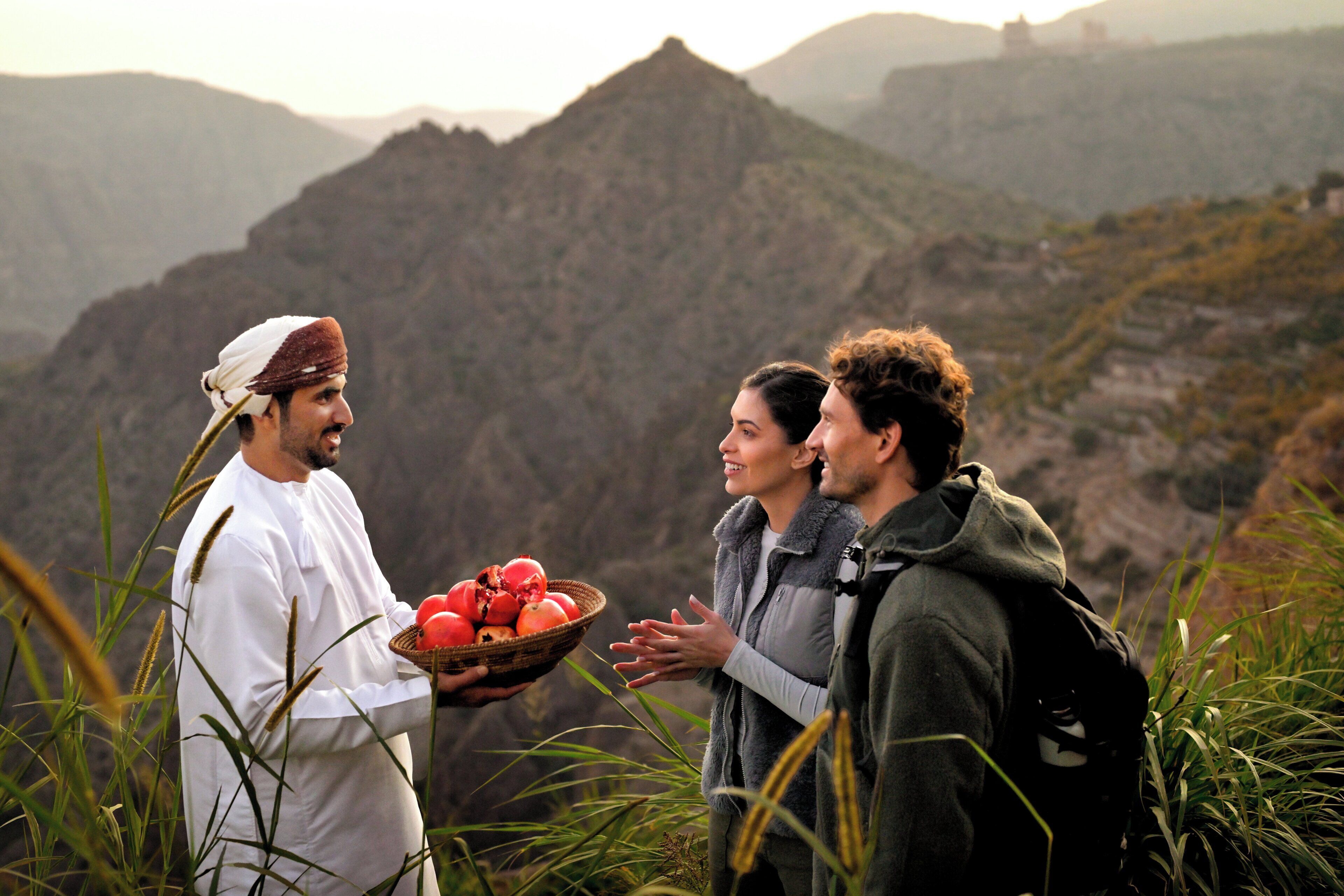 A person holding a basket of pomegranates in a mountainous area.