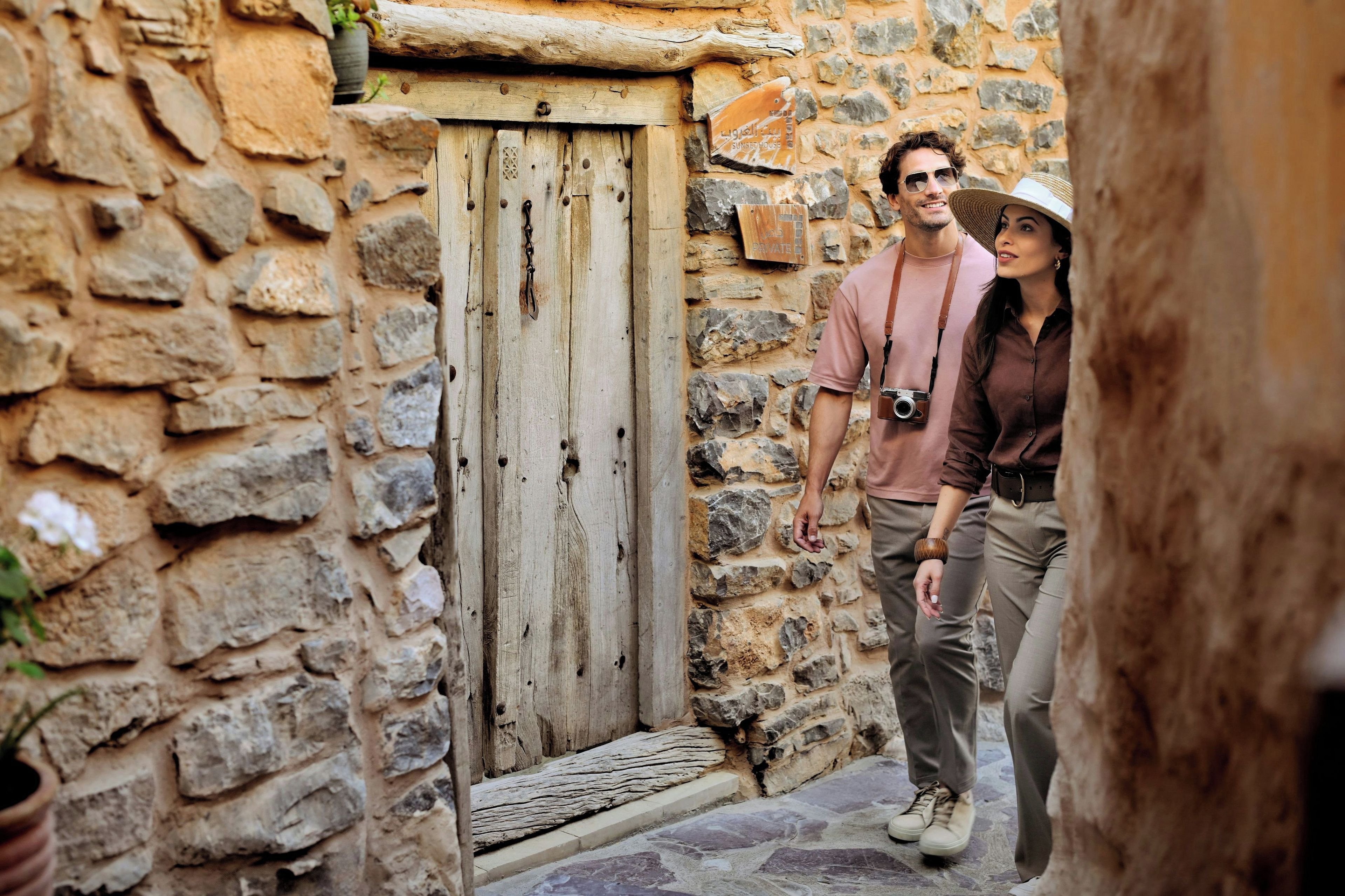 A narrow stone pathway leading to a wooden door with a metal handle, flanked by stone walls and a small potted plant.