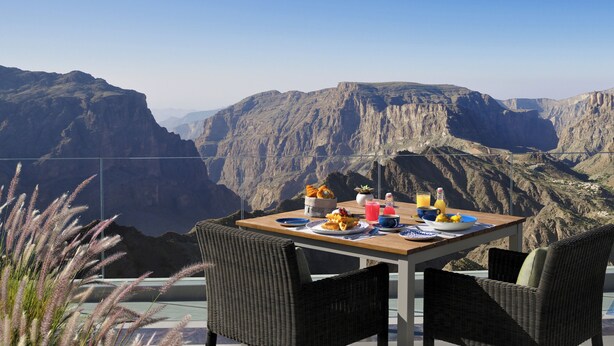 Een eettafel met uitzicht op een canyon, rieten stoelen en een bereid eten.