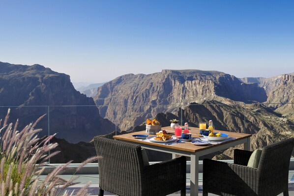Une table à manger avec vue sur un canyon, des chaises en osier et une table dressée.