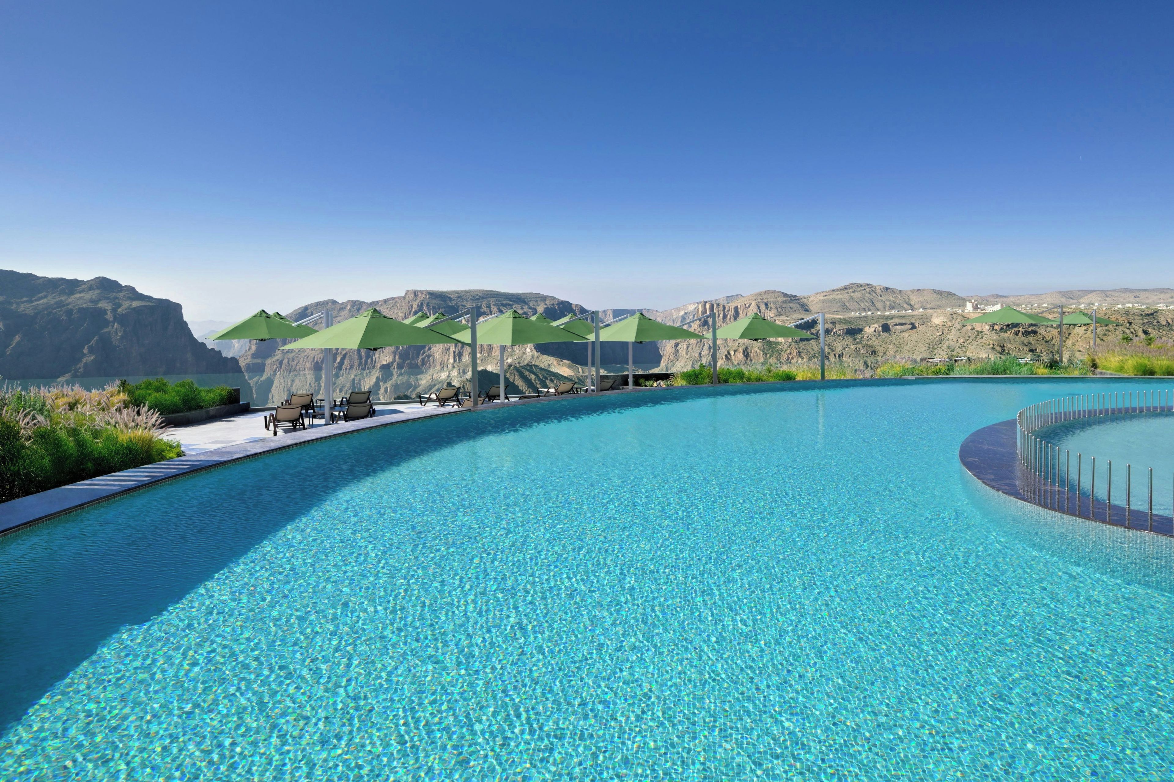Piscina infinita de color azul intenso con vistas a montañas y un cielo despejado.