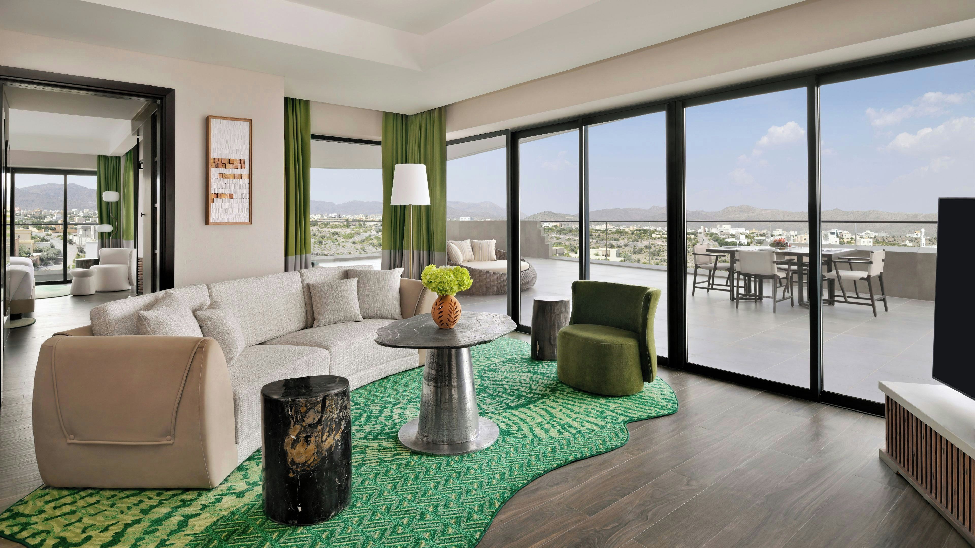 A modern living room with a sofa, armchairs, a coffee table, and a view of the cityscape through large windows.