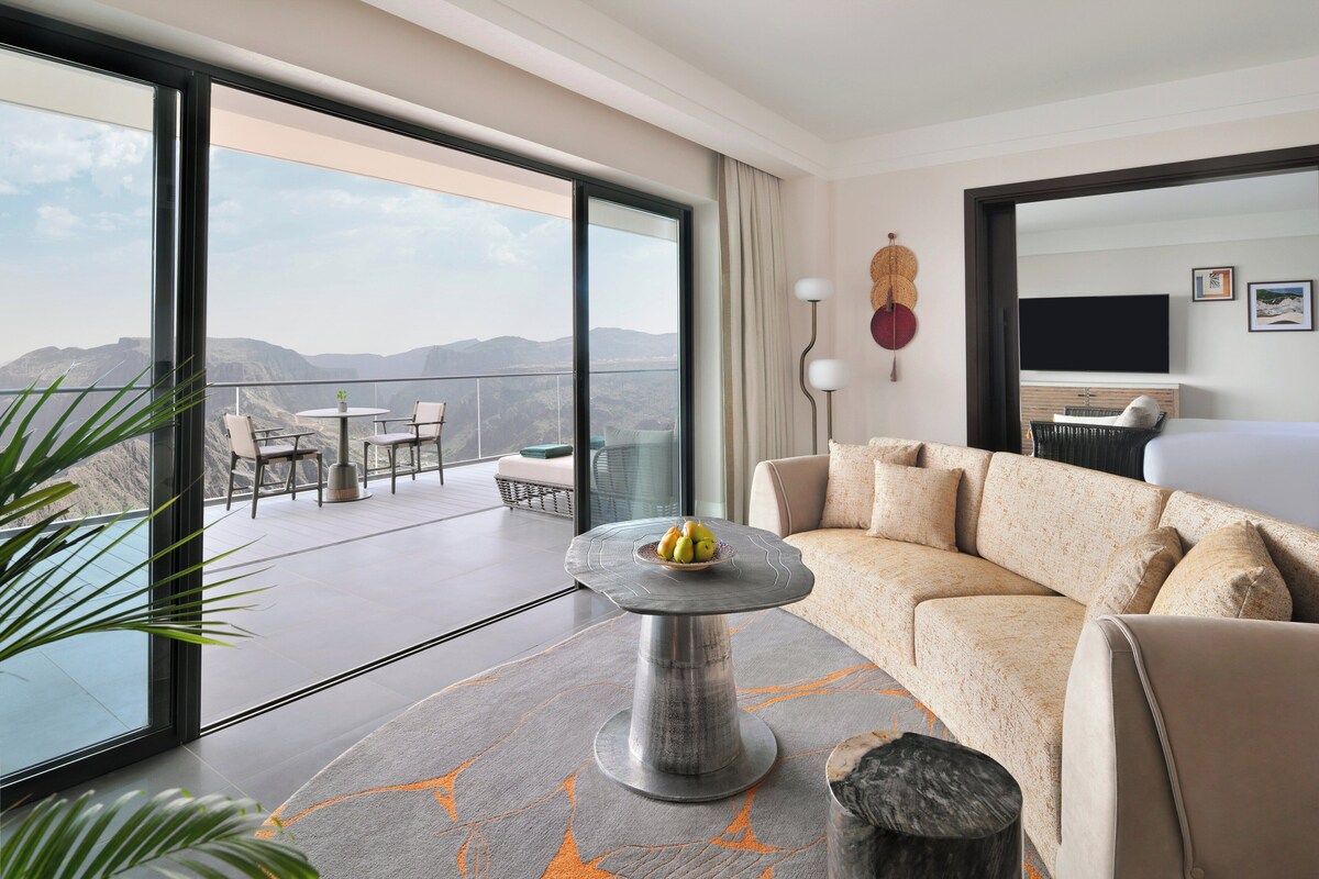 Een moderne hotelkamer met een ruim balkon, een ronde tafel met fruit, een bank en een televisie.