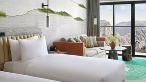 Een hotelkamer met een groot bed, een bank, een klein rond tafeltje en uitzicht op bergen door grote ramen.