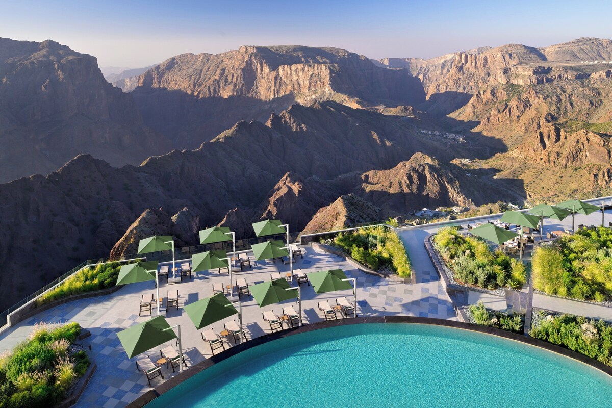 Un espace piscine doté de chaises longues et de parasols, entouré d’un paysage montagneux.