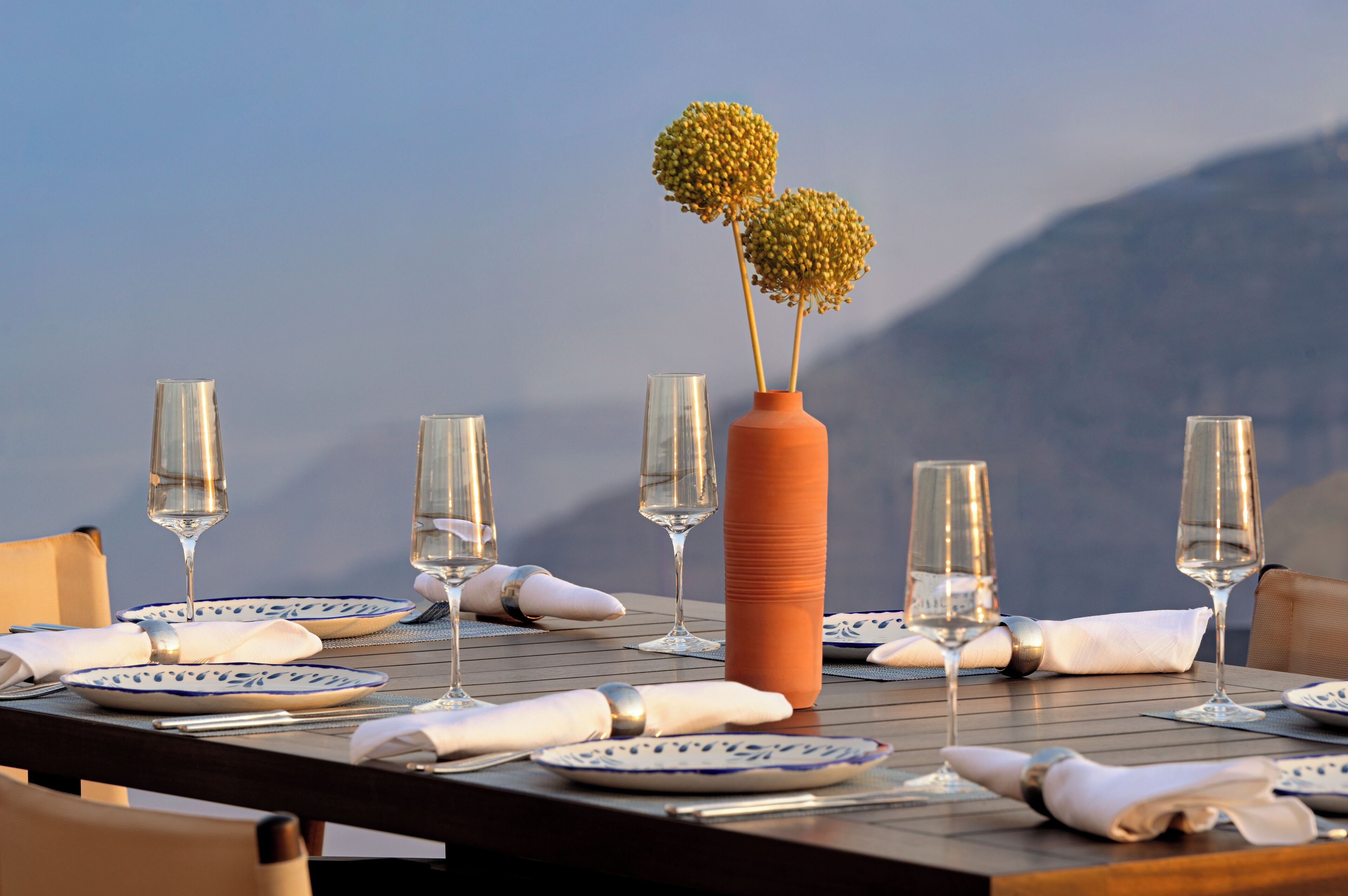 Una mesa dispuesta para una comida, con copas de vino, platos y un florero con flores.