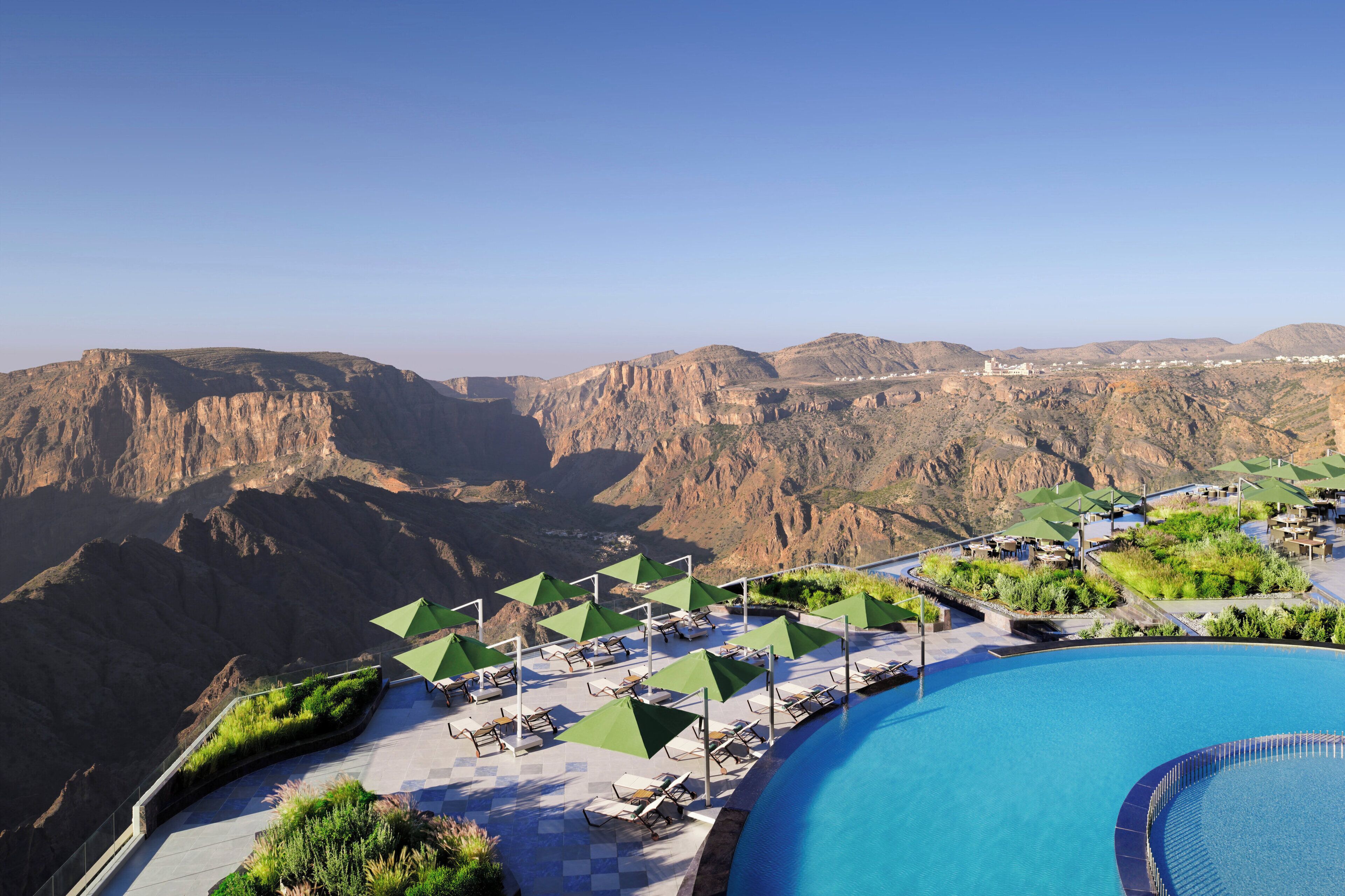Zona de piscina con sillones de descanso y sombrillas, con vistas a un paisaje montañoso.