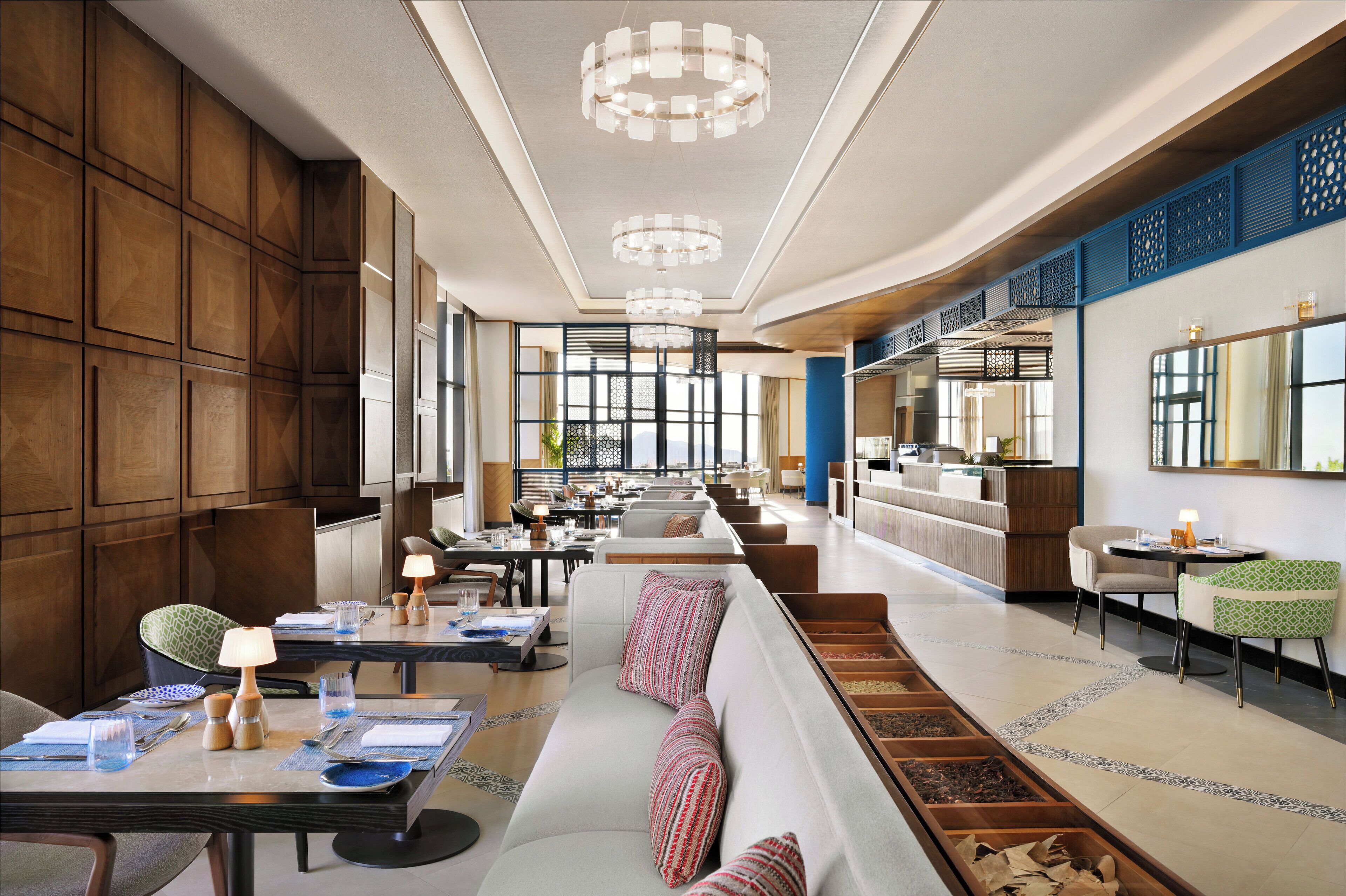 Un amplio vestíbulo de hotel con un sofá largo, mesas de comedor y una zona de cocina al fondo.