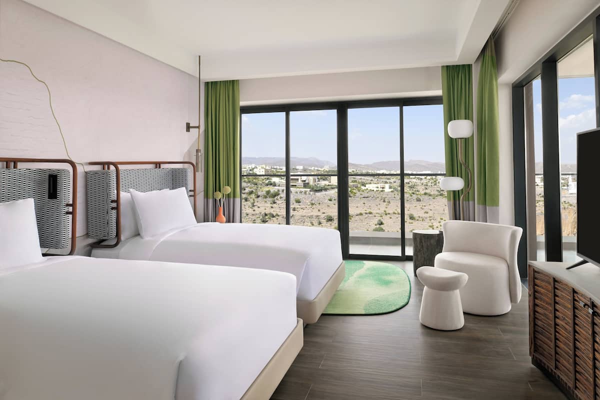 Une chambre d’hôtel avec deux lits, une télévision, une chaise et une vue sur un paysage désertique.
