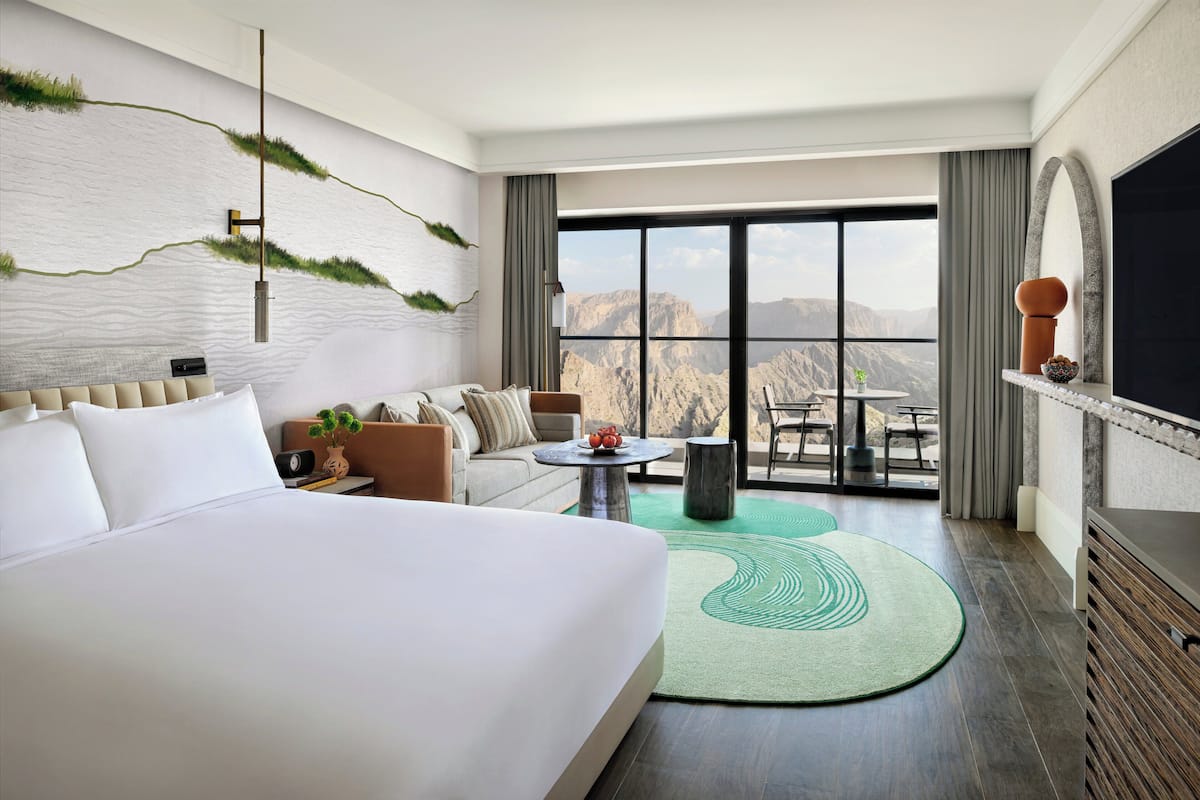 Une chambre d’hôtel avec un grand lit, un canapé, une petite table, une télévision et une vue sur les montagnes.