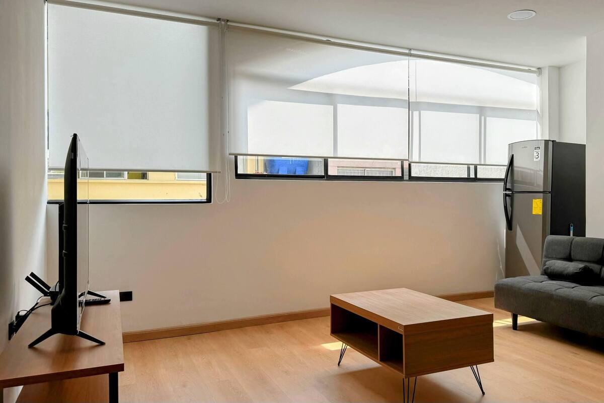 A modern living room with a sofa, a coffee table, a TV, and a refrigerator.