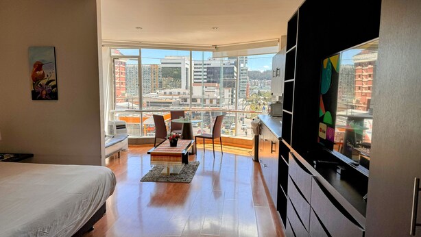A modern hotel room with a large balcony, a bed, a dining area, and a TV. - Edificio Tofino (Quito)