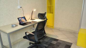 A workspace with a desk, two chairs, a laptop, a mouse, a lamp, and a yellow storage unit.