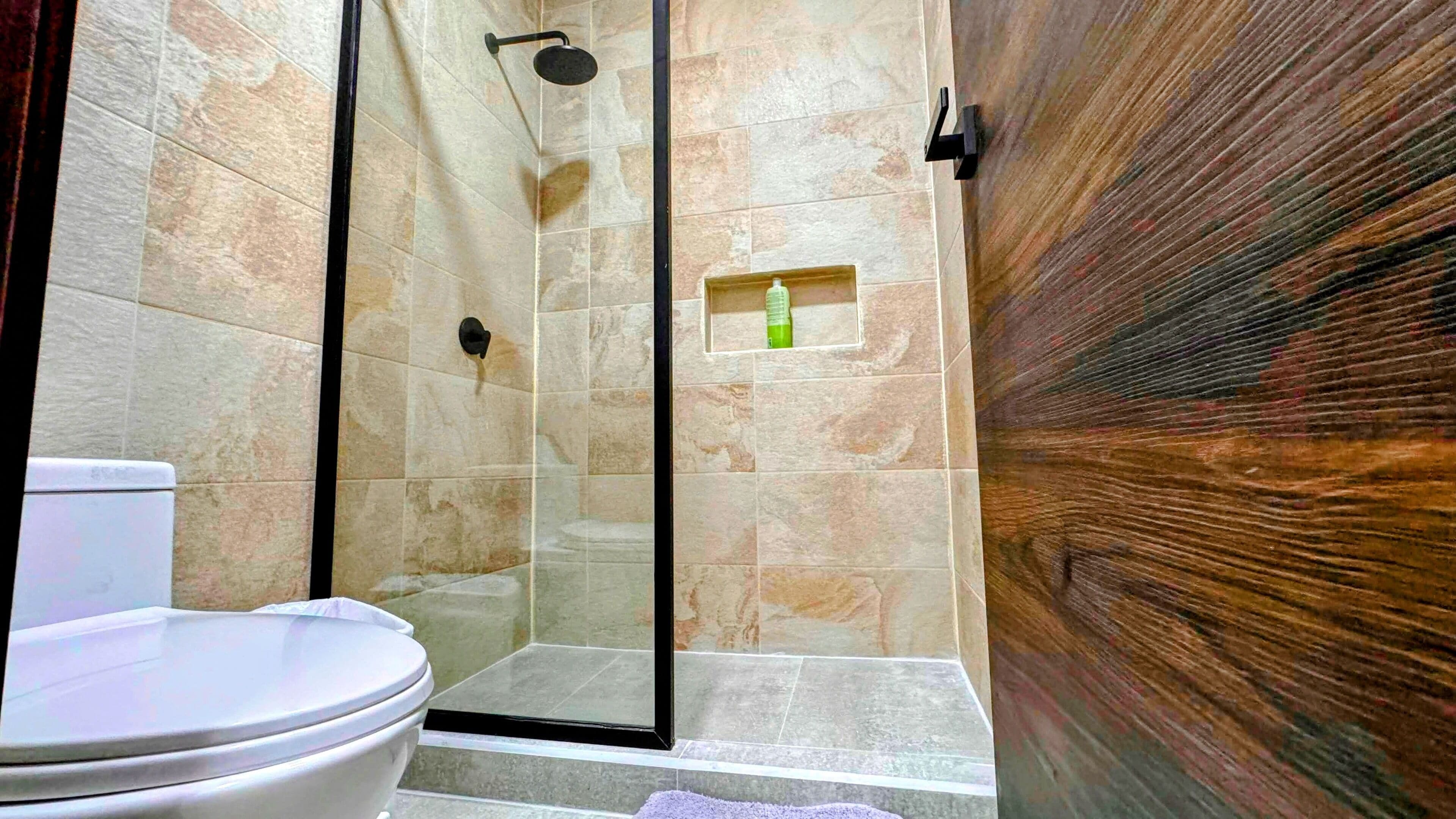 A bathroom with a shower, toilet, and a small shelf with a bottle.